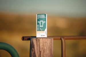 A phone tempered glass screen protector product package sits on a rustic wooden post at sunset.