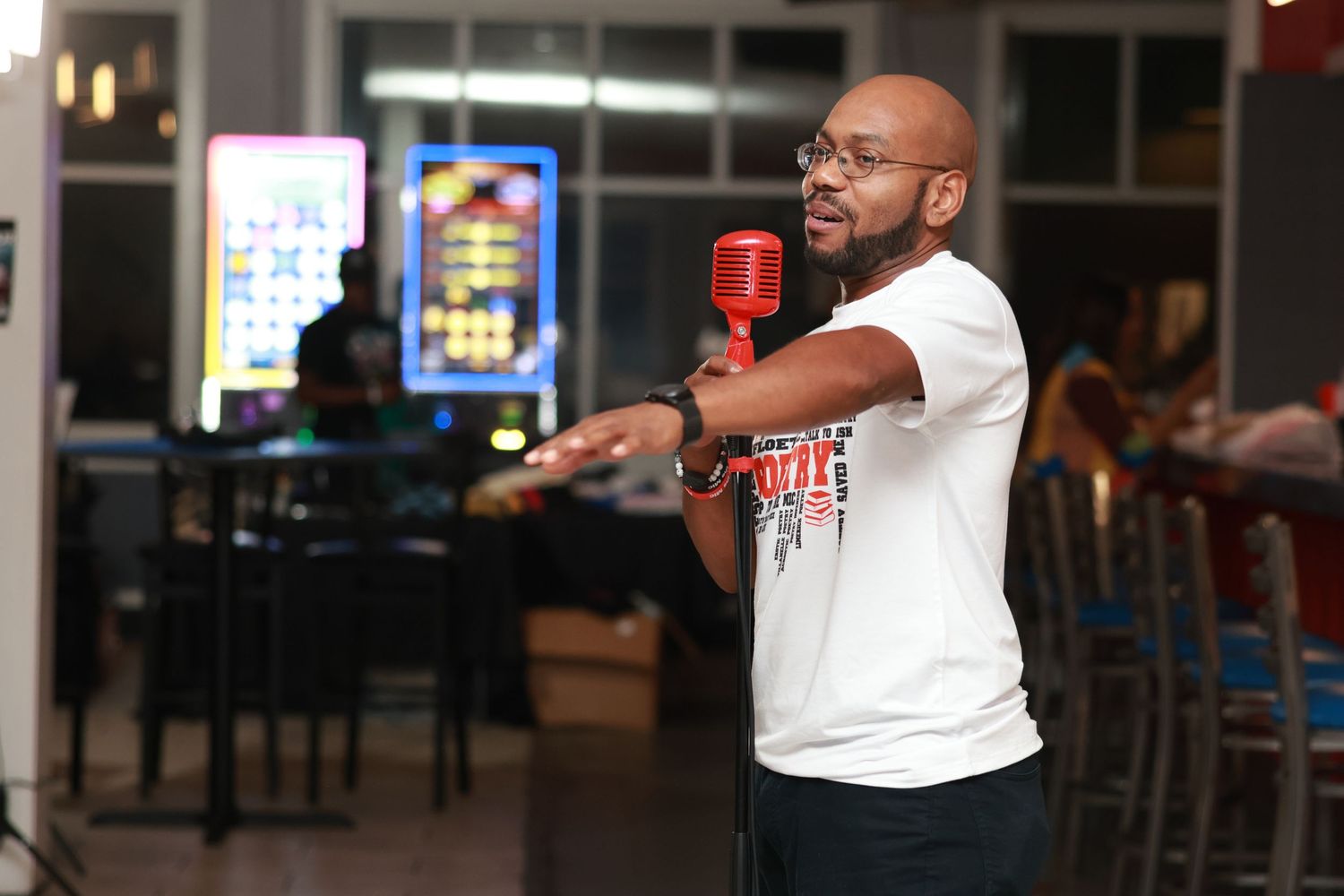 Person in white t-shirt gesturing while speaking at a bar or restaurant venue.