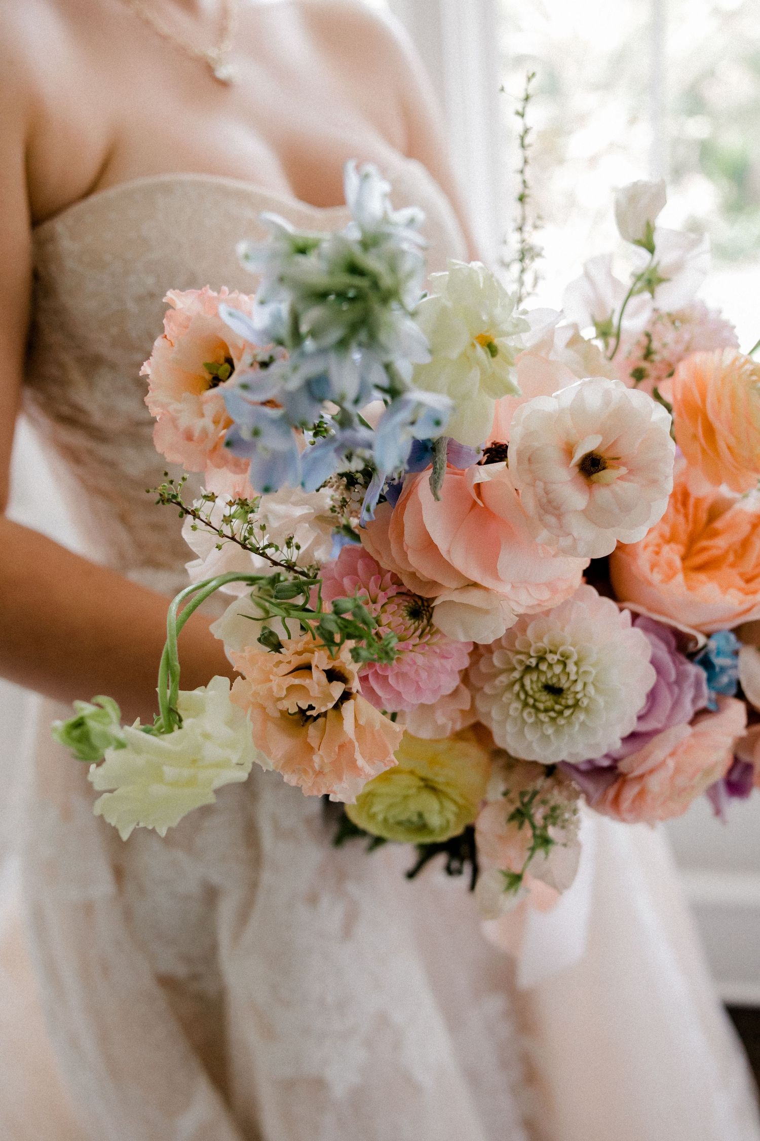 A romantic peach and cream wedding bouquet with roses and ranunculus rests on white fabric.