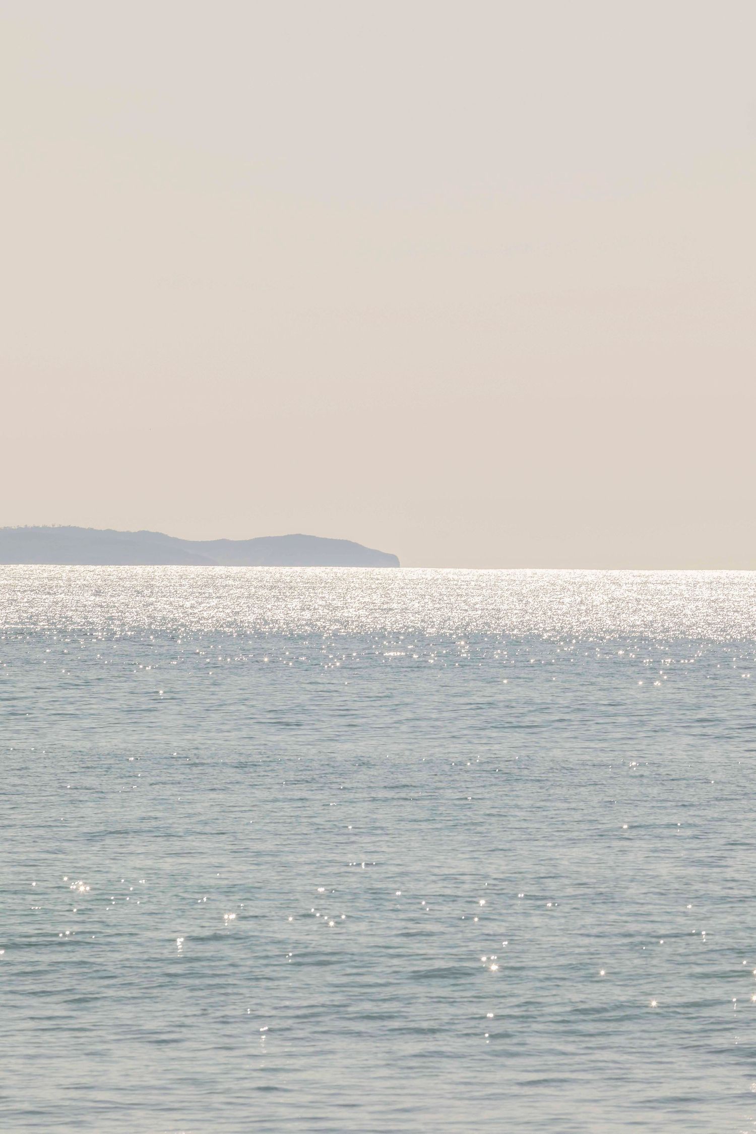 Sparkling ocean waters with distant mountains under a hazy sky.