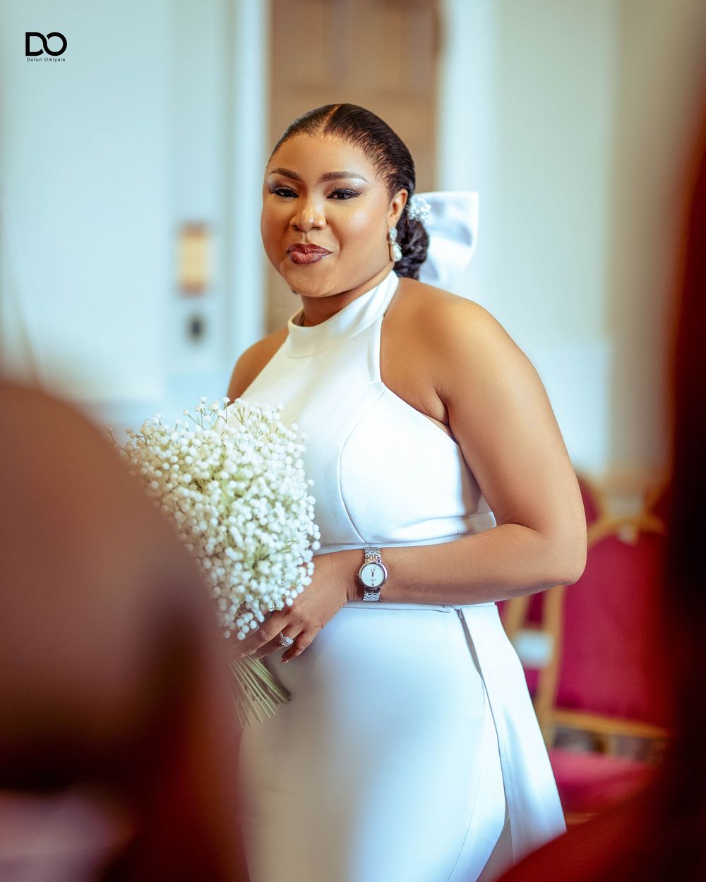 A person in a white dress holding a bouquet of baby's breath flowers in an indoor setting.