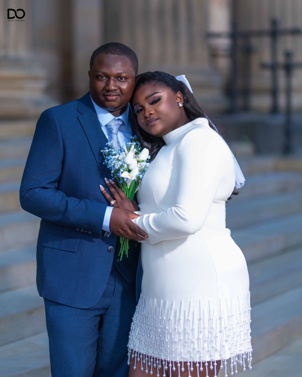 Newlywed couple in navy suit and white dress share intimate moments during outdoor wedding photoshoot.