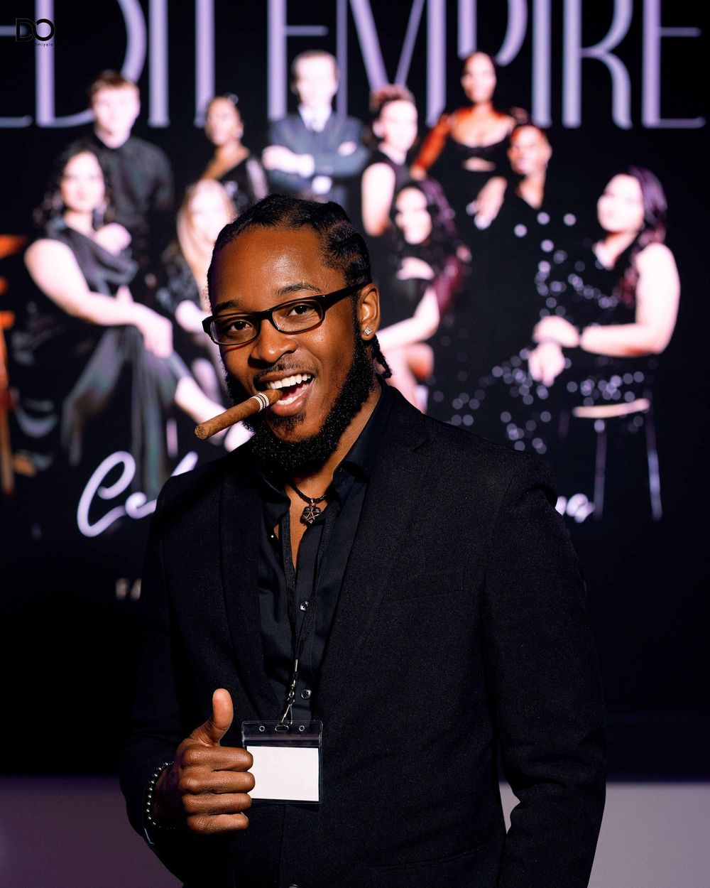 Guest in black suit gives thumbs up while posing at Empire fashion event.