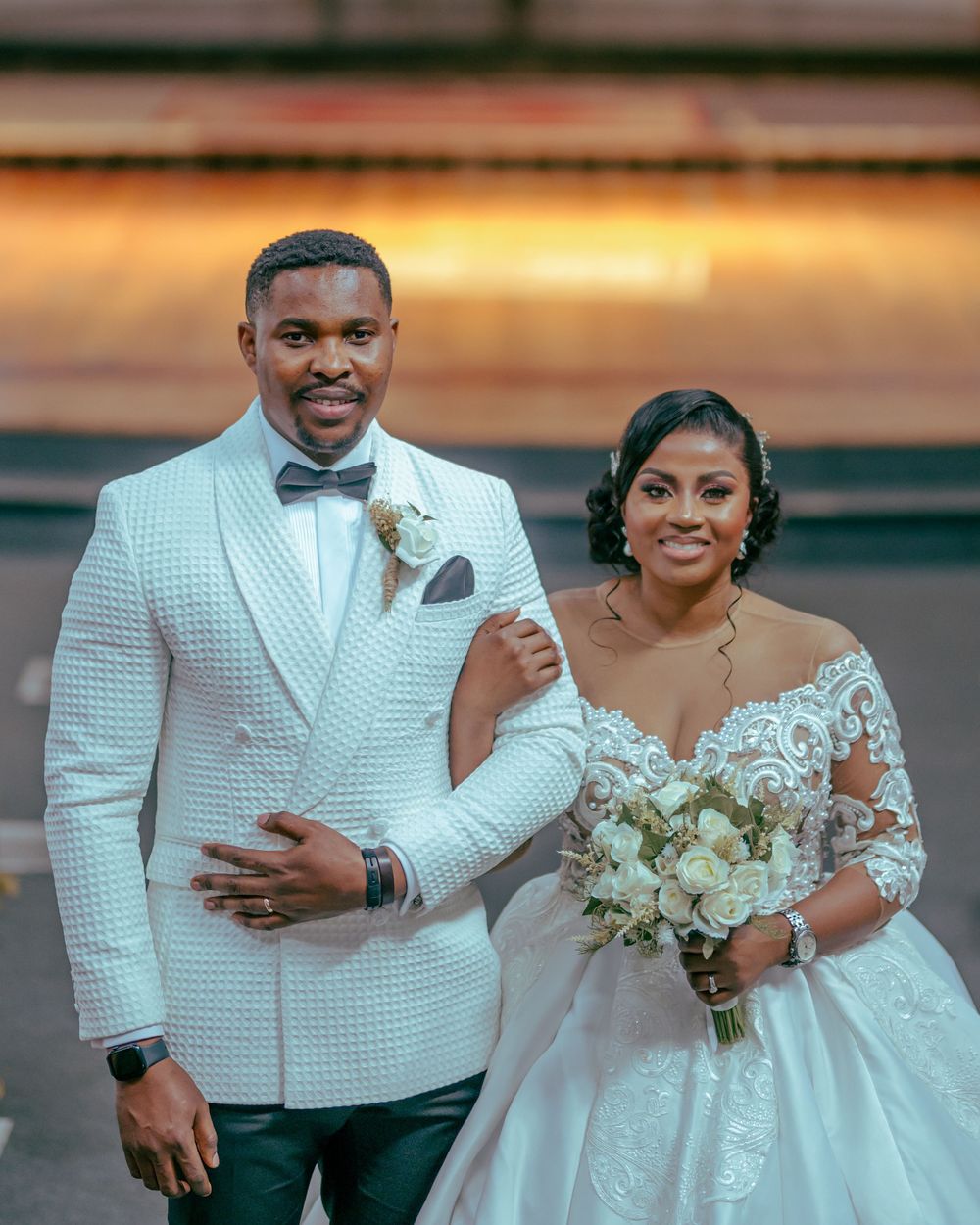 A happy couple in elegant white wedding attire smile and pose together during their wedding celebration.