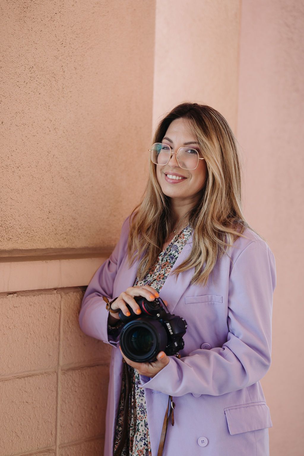 Woman in floral dress and hat posing with phone against pink columns.