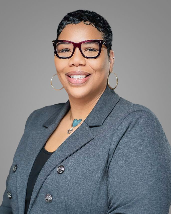Professional headshot of Client wearing glasses and a grey blazer, smiling warmly against a neutral background. Kelly Photography Atlanta