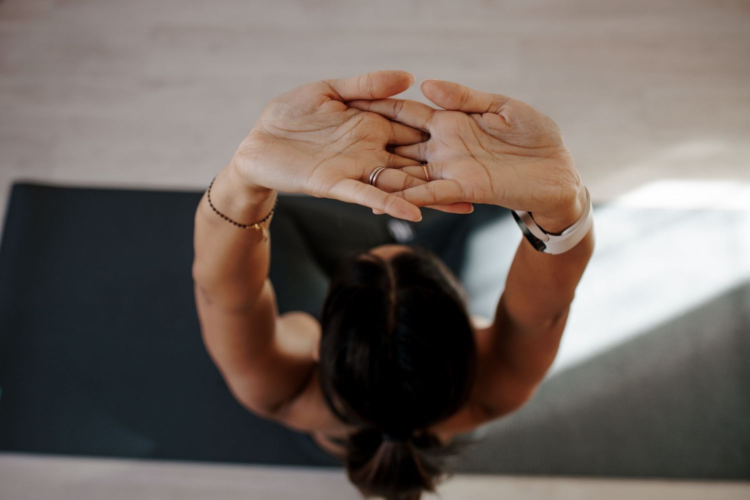 Overhead view of a woman practicing yoga with hands clasped above her head on a mat.