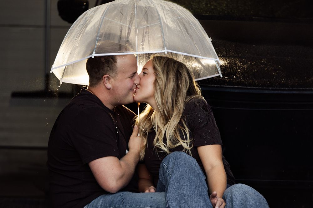 A couple shares a romantic kiss under a clear umbrella in the rain at night.