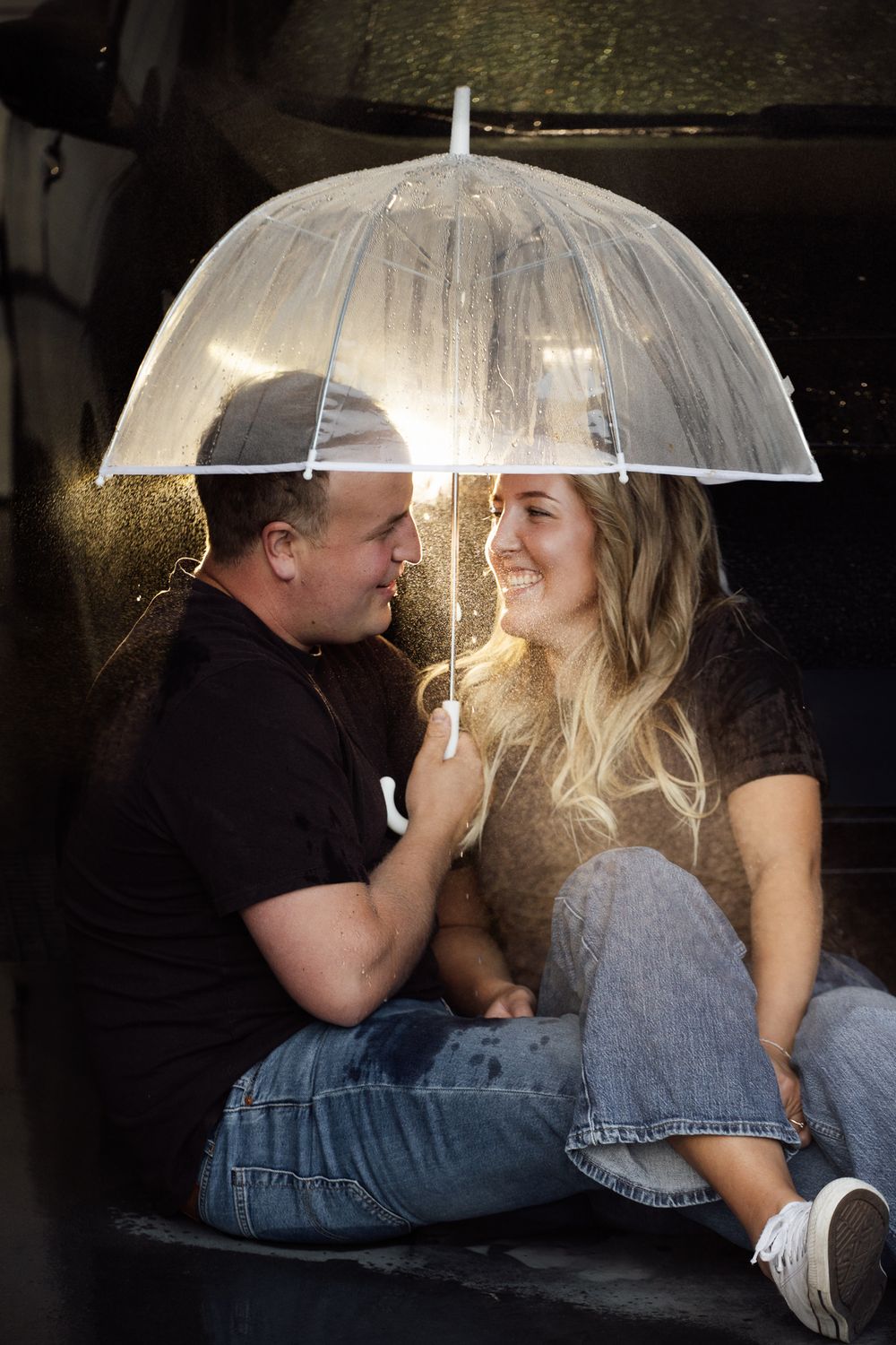Couple sharing a romantic moment under a clear bubble umbrella in the rain, smiling at each other.