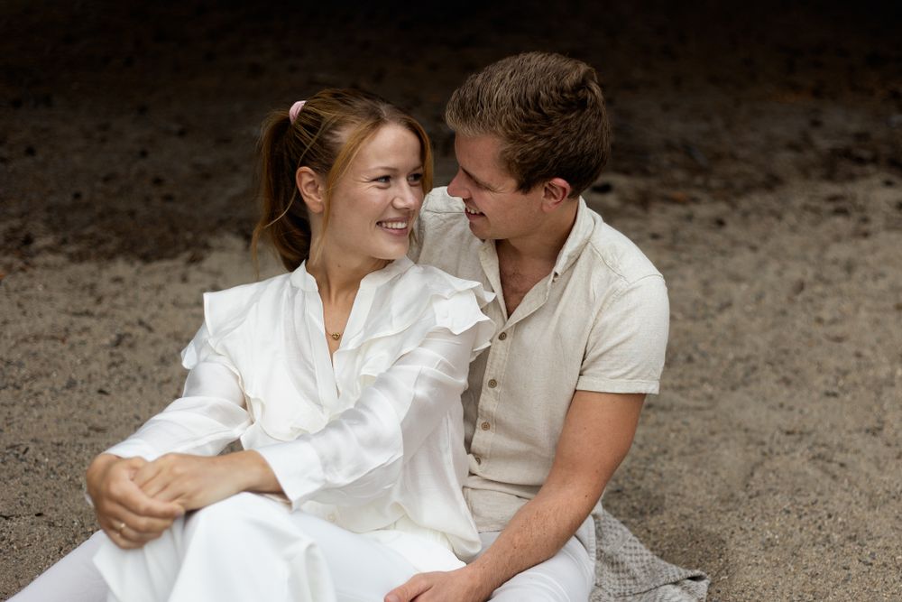 Romantic couple in white outfits embraces on sandy beach.