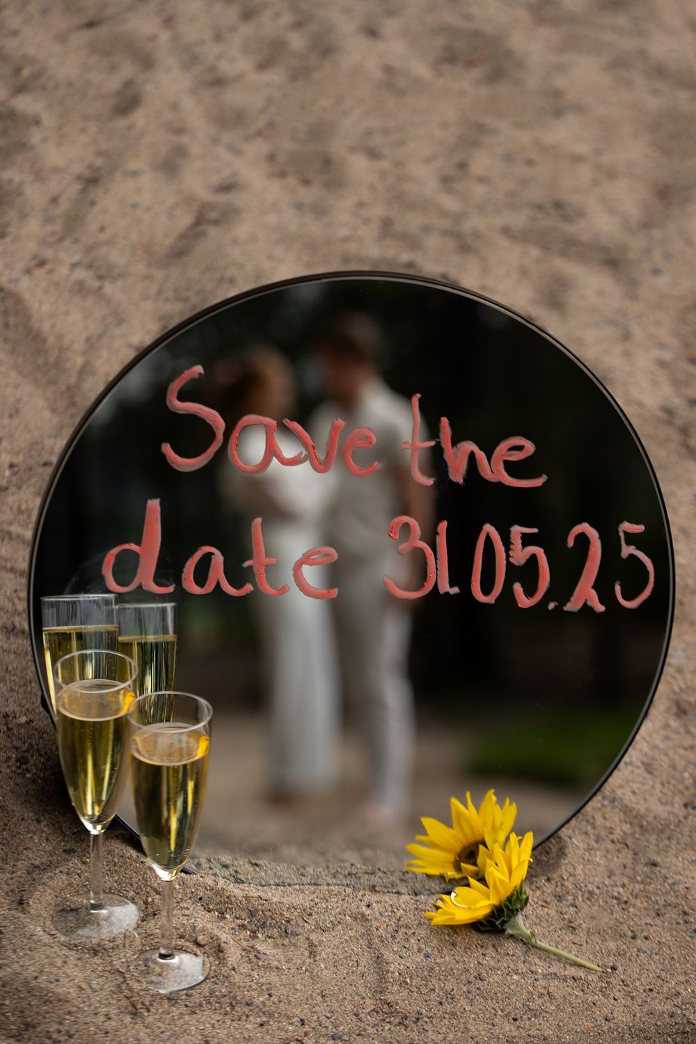 Save the date message written on mirror with champagne glasses and sunflower decoration.