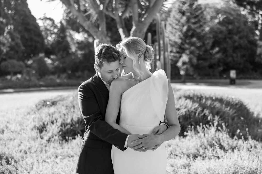 Black and white wedding portrait captured in sunlit garden setting.