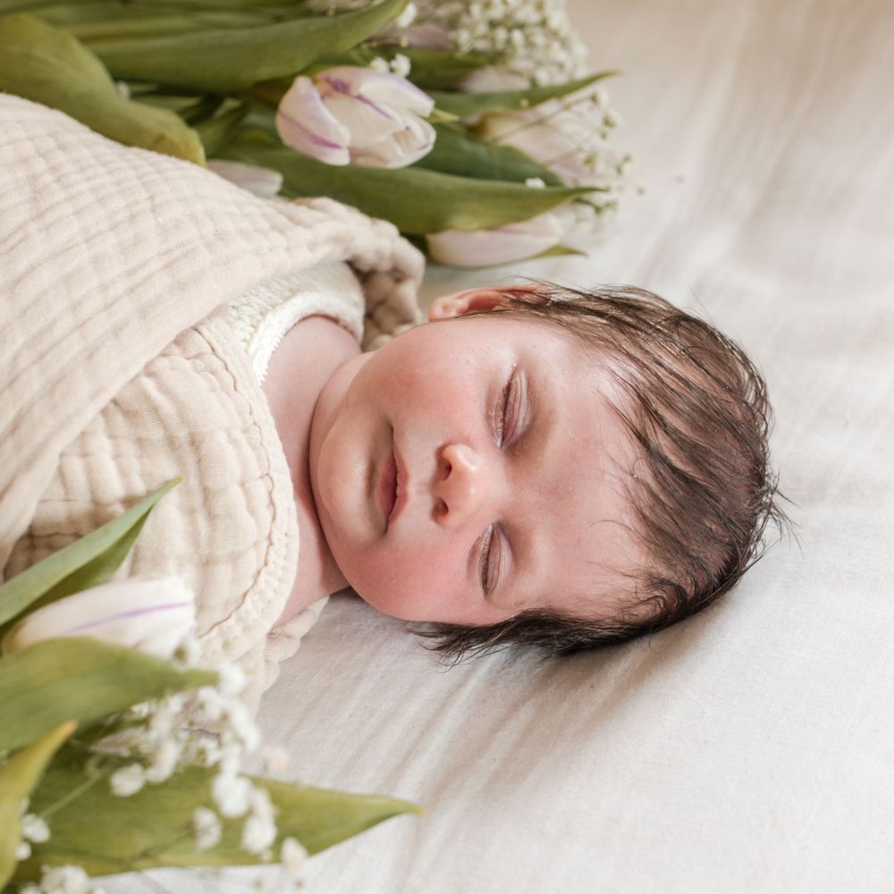 A sleeping baby wrapped in cream colored fabric surrounded by green tulips and baby's breath flowers.