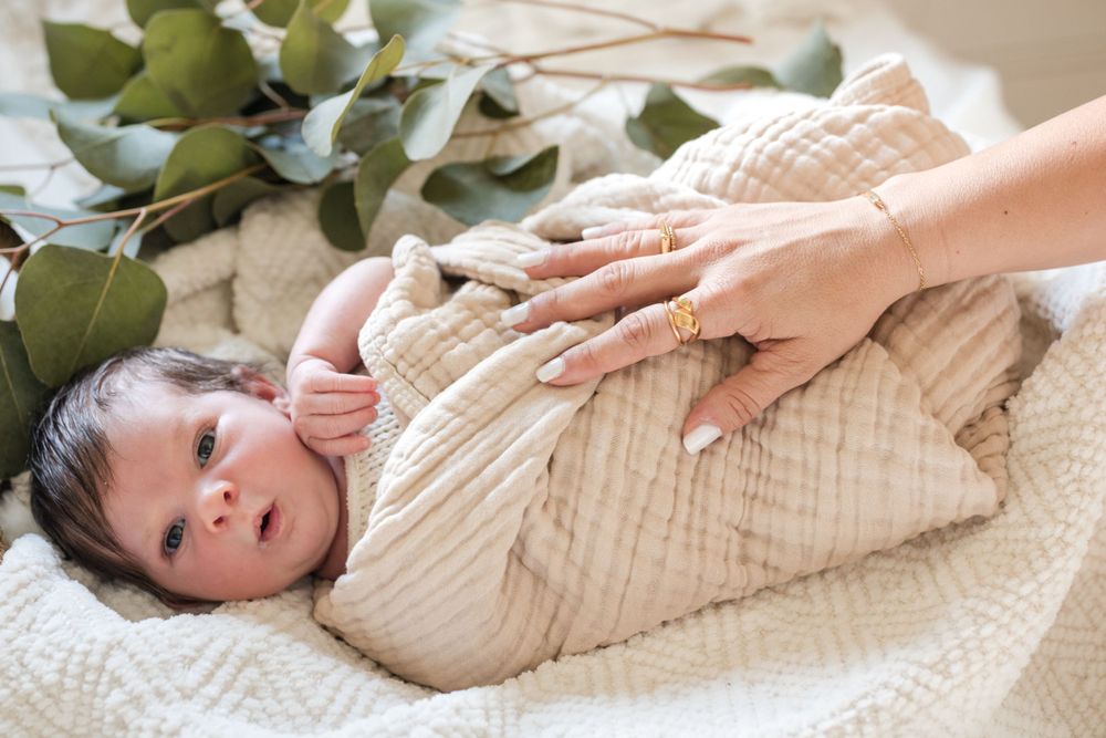 A swaddled newborn lying on white bedding with eucalyptus leaves as decoration.