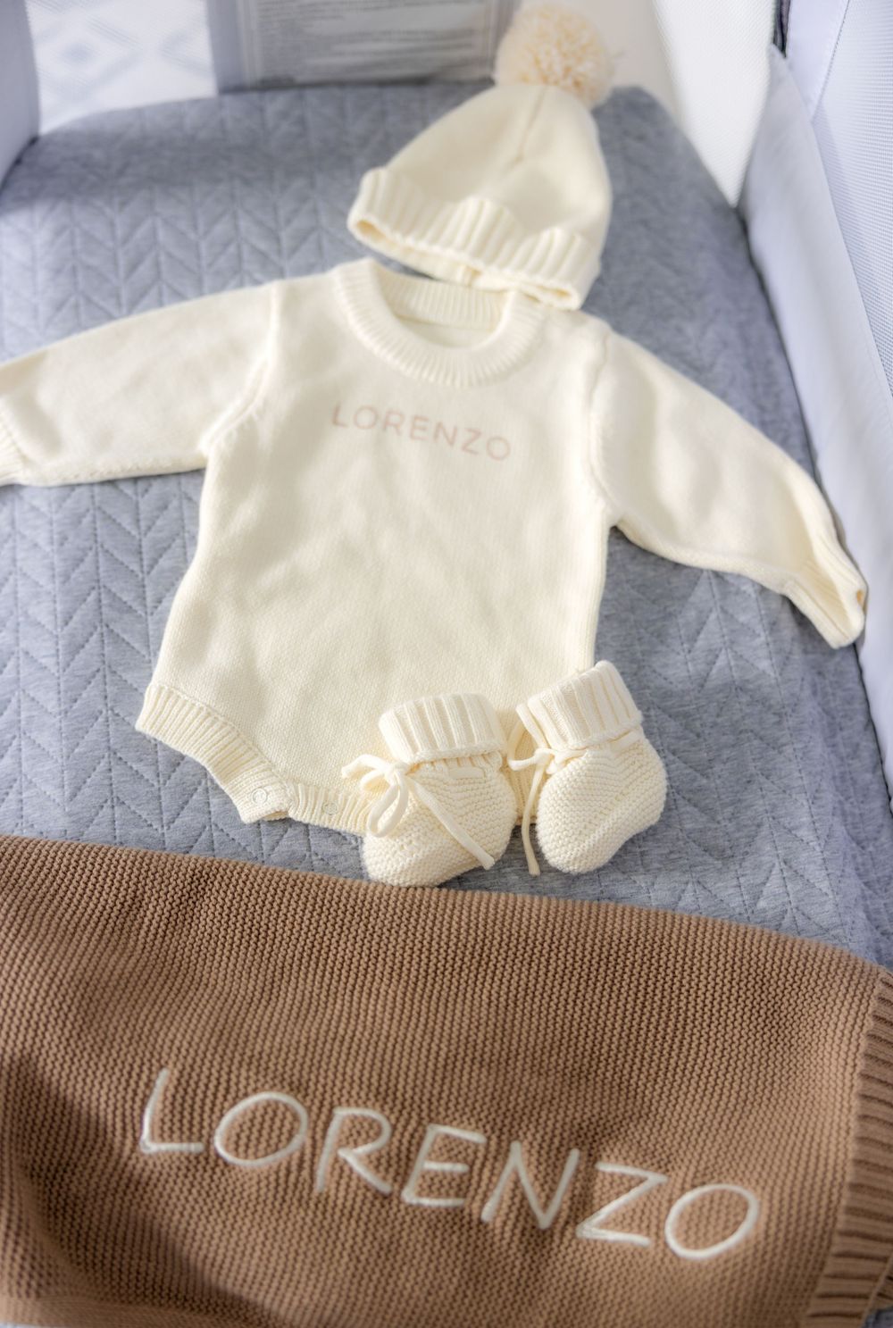 Personalized baby set named Lorenzo, cream knit romper, pom-pom hat, booties, and tan blanket.
