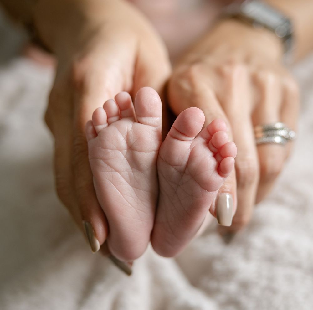 Adult hands gently cradling tiny newborn baby feet, showcasing delicate toes and soft skin in a tender close-up photo.