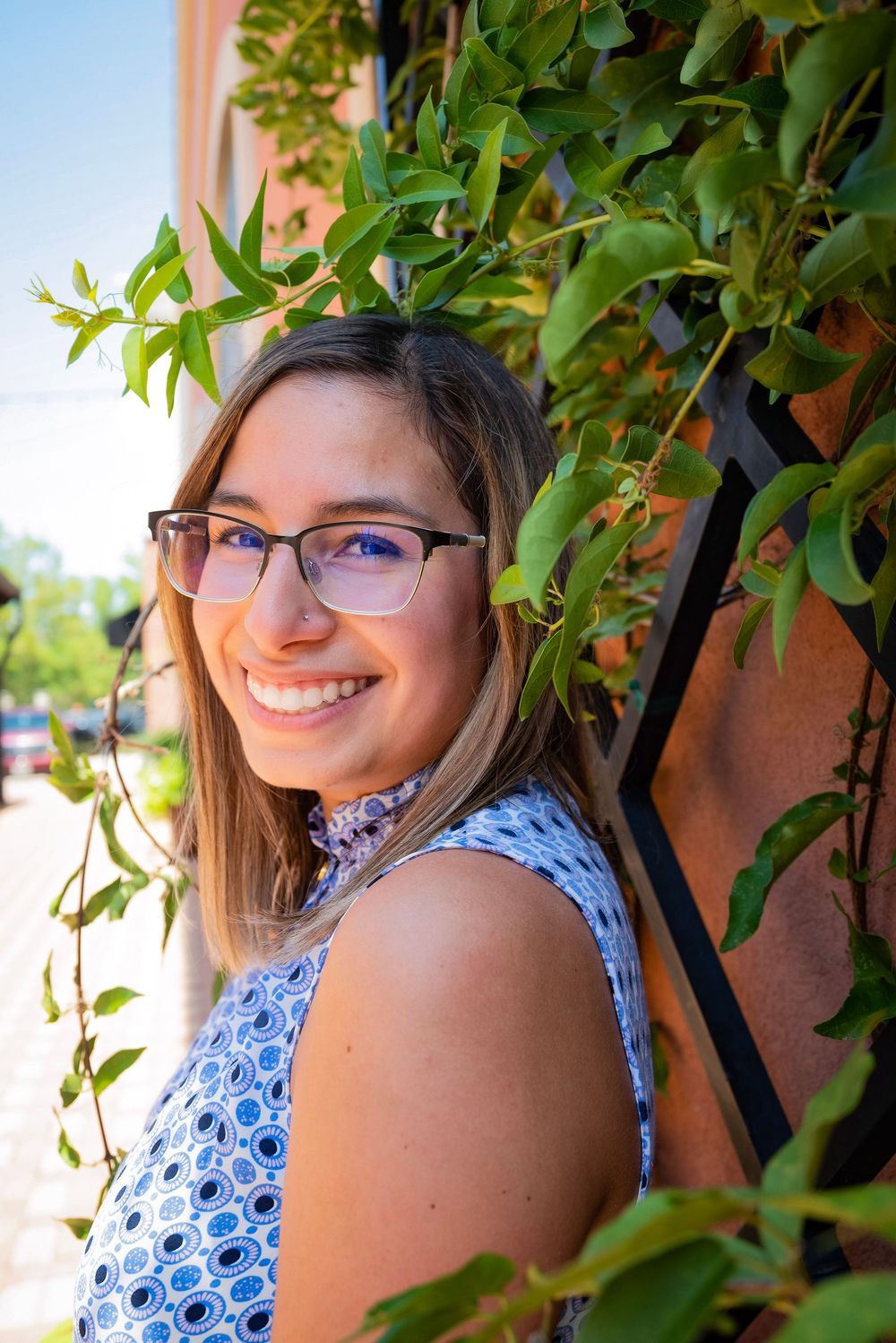 A person in glasses and a blue floral dress poses outdoors among green foliage in a series of casual portrait shots.