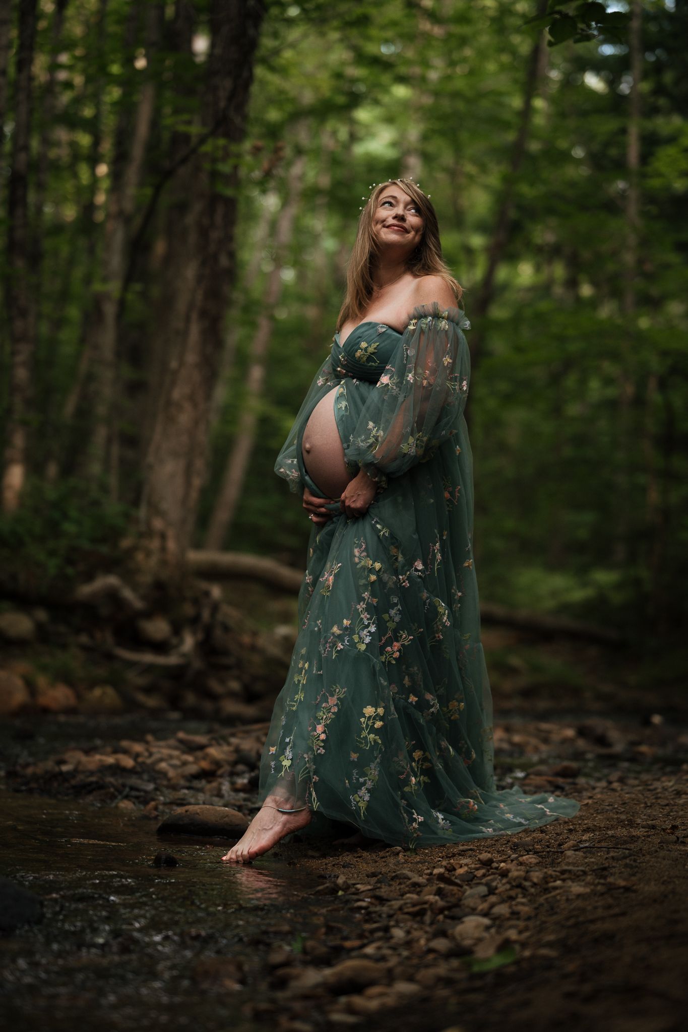 A pregnant lady stands in a dreamy forest brook holding her belly