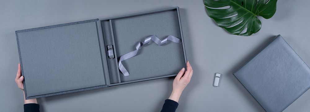 Gray wedding album being opened on a desk with a tropical leaf decoration.