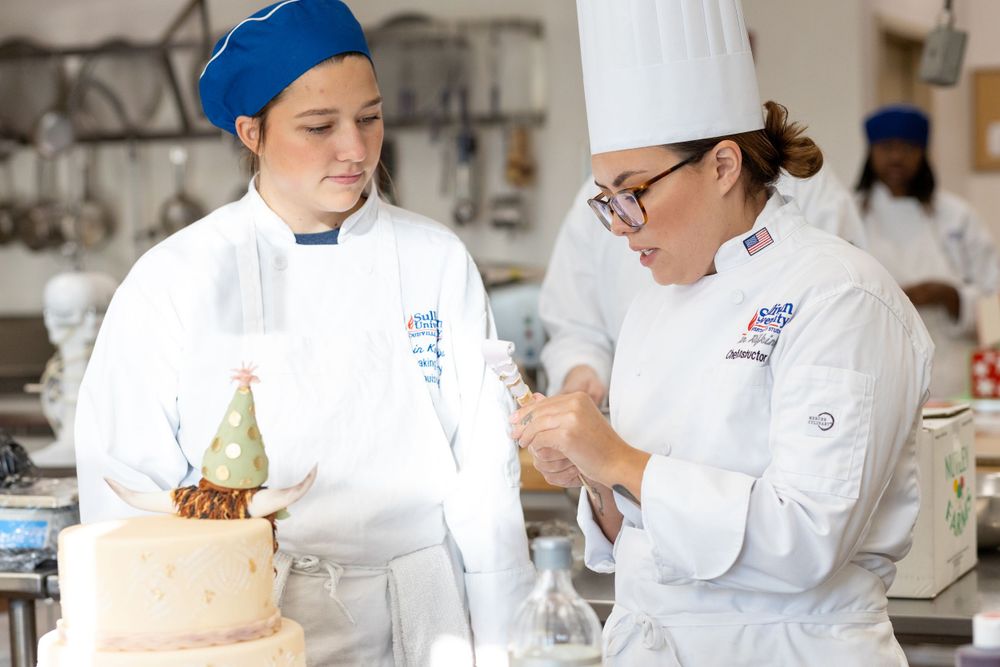 Chef Instructor coaching her student towardsadding the finishing touches to a cake