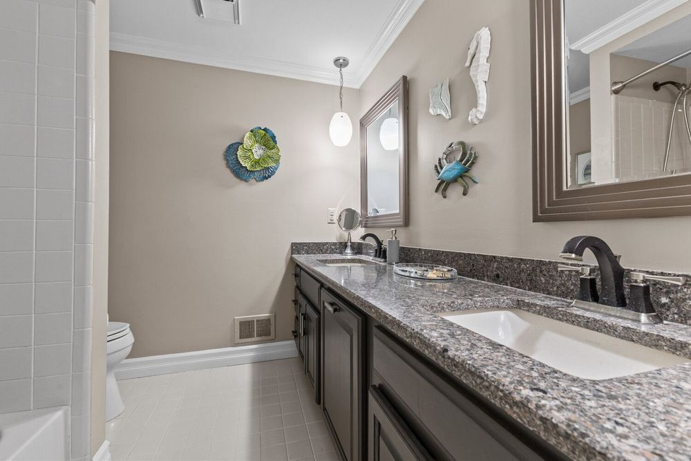 Elegant bathroom featuring double granite countertop vanity with dark cabinets, crown molding, and tiled shower.