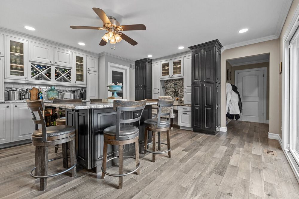 Elegant kitchen with dark island, white cabinetry, glass-front upper cabinets, bar seating, and hardwood floors.