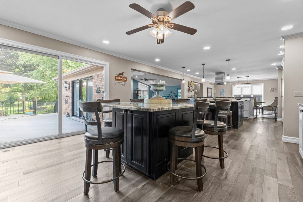 Open-concept kitchen featuring large dark island with bar seating, hardwood floors, and sliding doors to outdoor deck.
