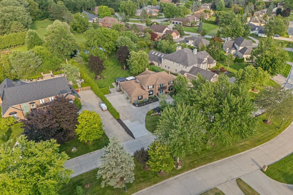 Aerial view of a large brick estate home surrounded by mature trees in an upscale suburban neighborhood.