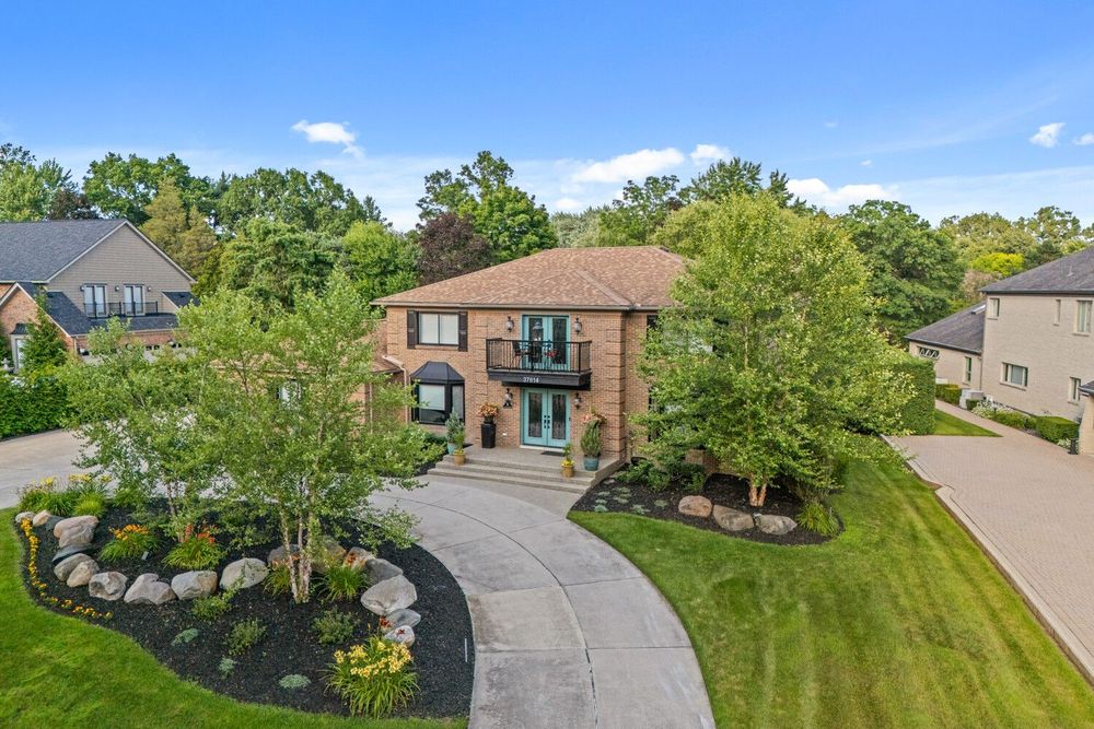 Elegant brick two-story home featuring a curved driveway, lush lawn, and professionally designed landscaping.