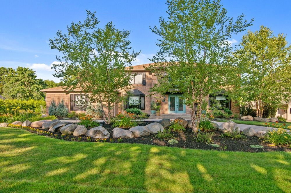 Luxurious estate home with teal front door, stone boulder landscaping, and manicured green lawn at dusk.