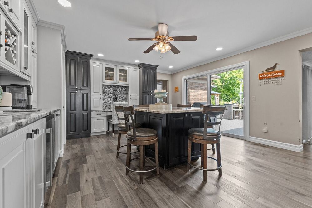 Open kitchen with dark island seating, gray cabinetry, hardwood floors, and sliding door to backyard patio.