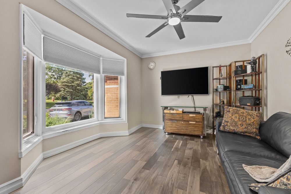 Cozy living room with hardwood floors, bay window, ceiling fan, wall-mounted TV, and leather sofa.