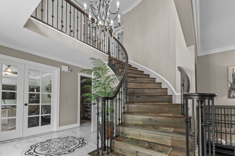 Elegant two-story foyer featuring curved wooden staircase with wrought iron balusters and decorative tile flooring.