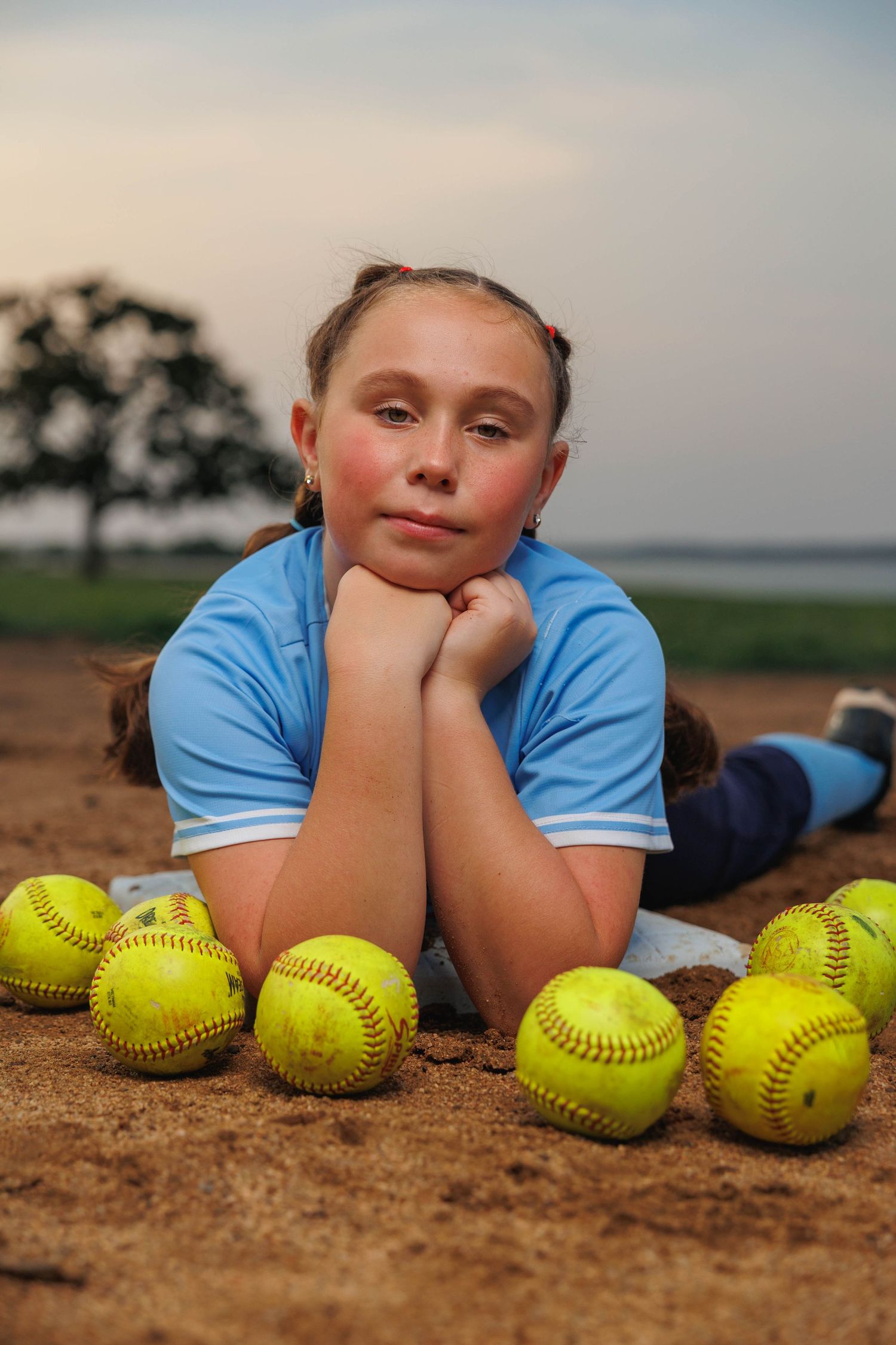 Softball player rests on ground with collection of yellow softballs.