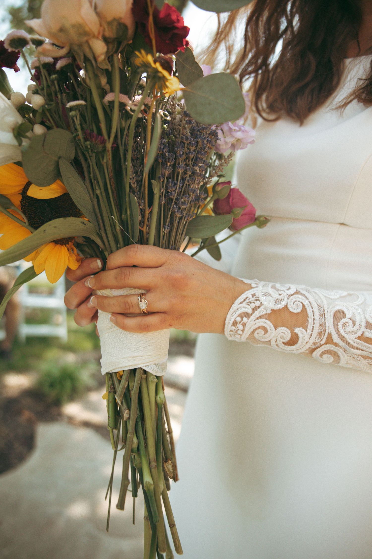 Close-up of lace sleeve wedding dress detail and wildflower bouquet with engagement ring.