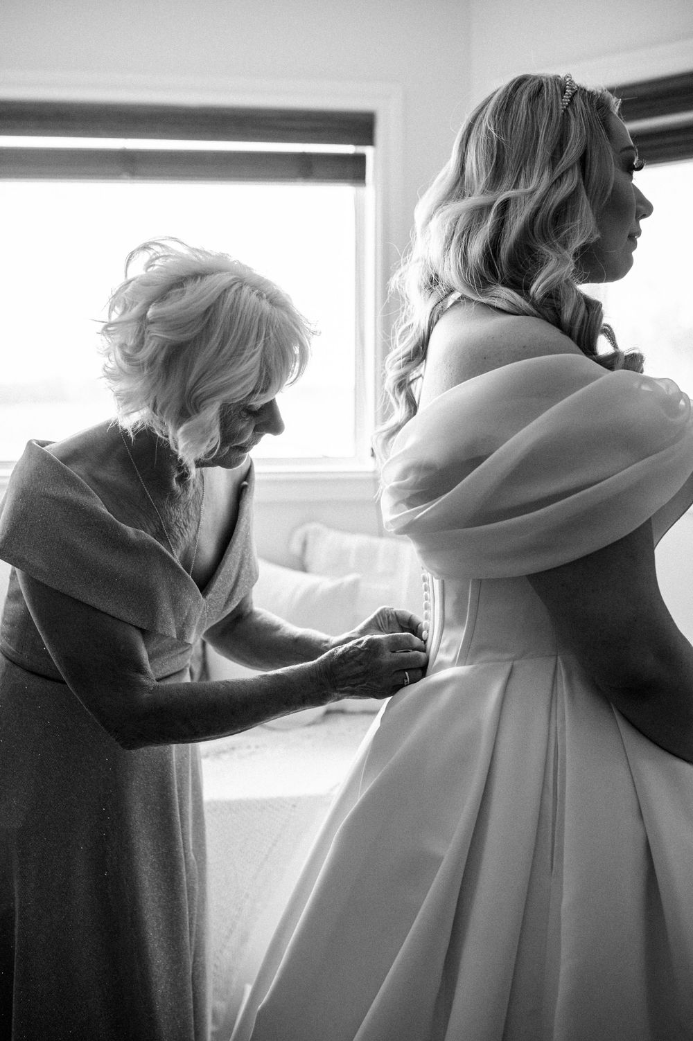 A touching black and white moment of dress preparation between two people on the wedding day.