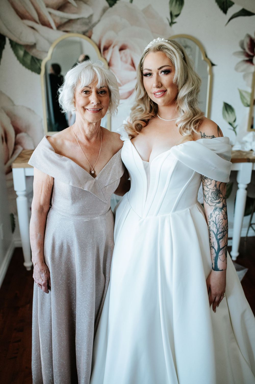 A wedding moment in a stylish room with floral wallpaper featuring two people in elegant dresses.