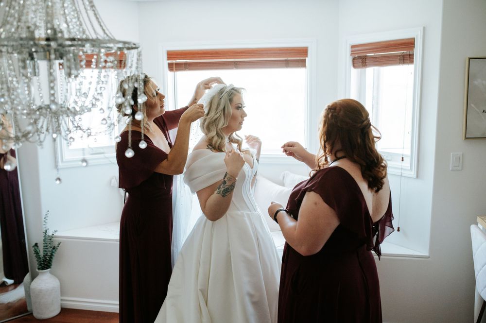A wedding preparation scene with multiple people helping with the white dress under a chandelier.