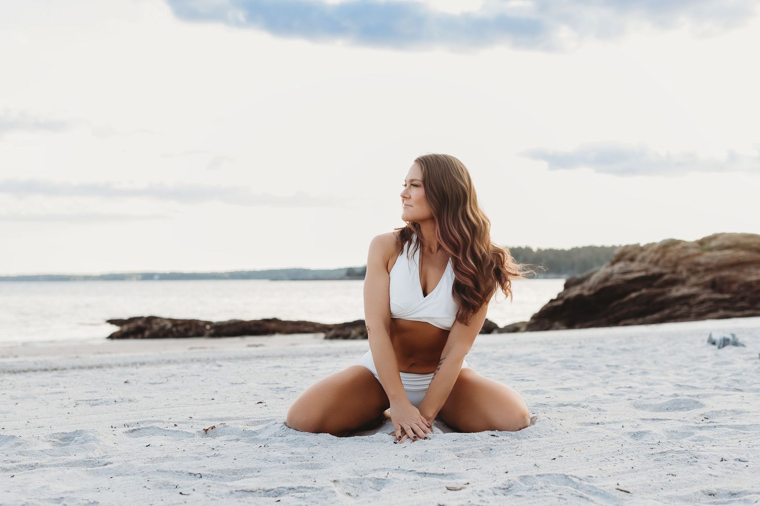 Woman in a white bathing suit posing on Pemaquid Beach in Bristol, Maine, during a warm summer sunset.