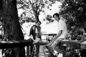 young man and teenage boy lean on wooden bridge in woods looking at camera, captured in 35mm b/w film by kansas city photographer
