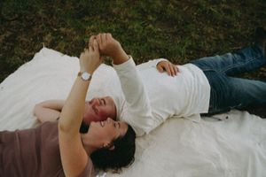 Engaged couple of man and woman lay on a quilt holding hands and smiling.