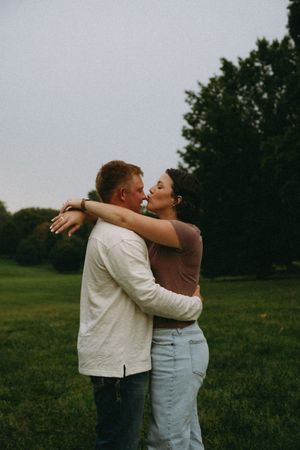 Woman kisses man on nose in tree landscape.