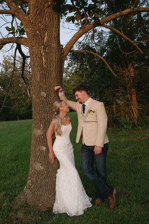 bride and groom lean on tree smiling at each other.