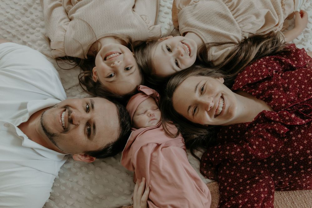 Overhead view of a happy family of five lying in a circle on a white blanket, smiling up at the camera.