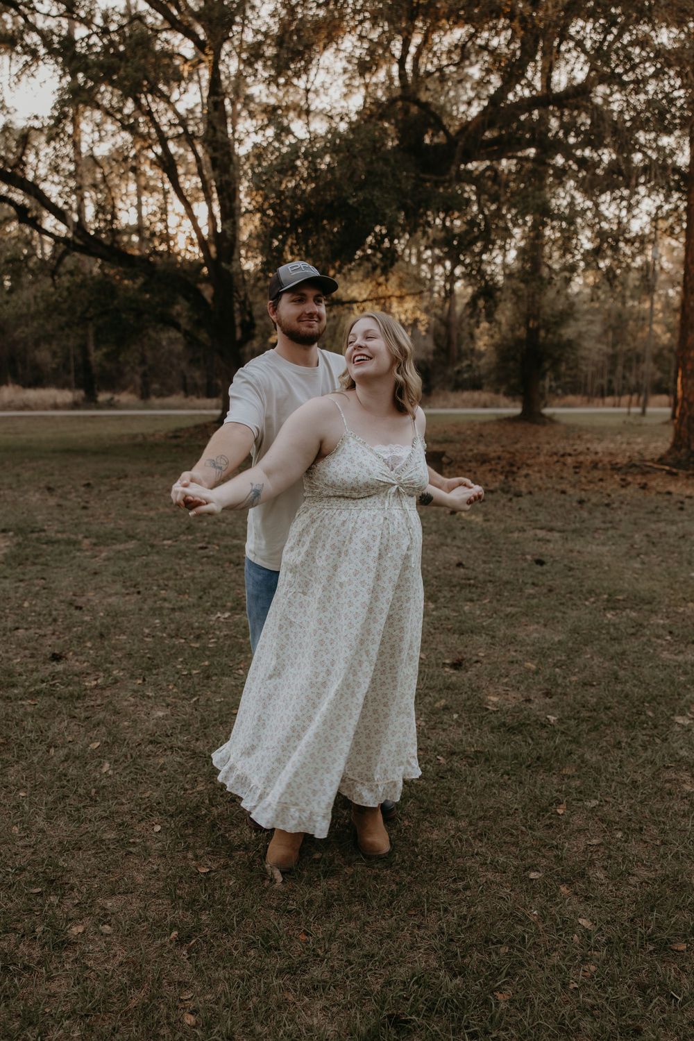 A joyful couple dances outdoors in a park, woman in floral dress, man in cap and jeans, golden hour light.