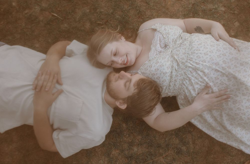 Two children lying on the ground outdoors, smiling and cuddling together in soft natural light.