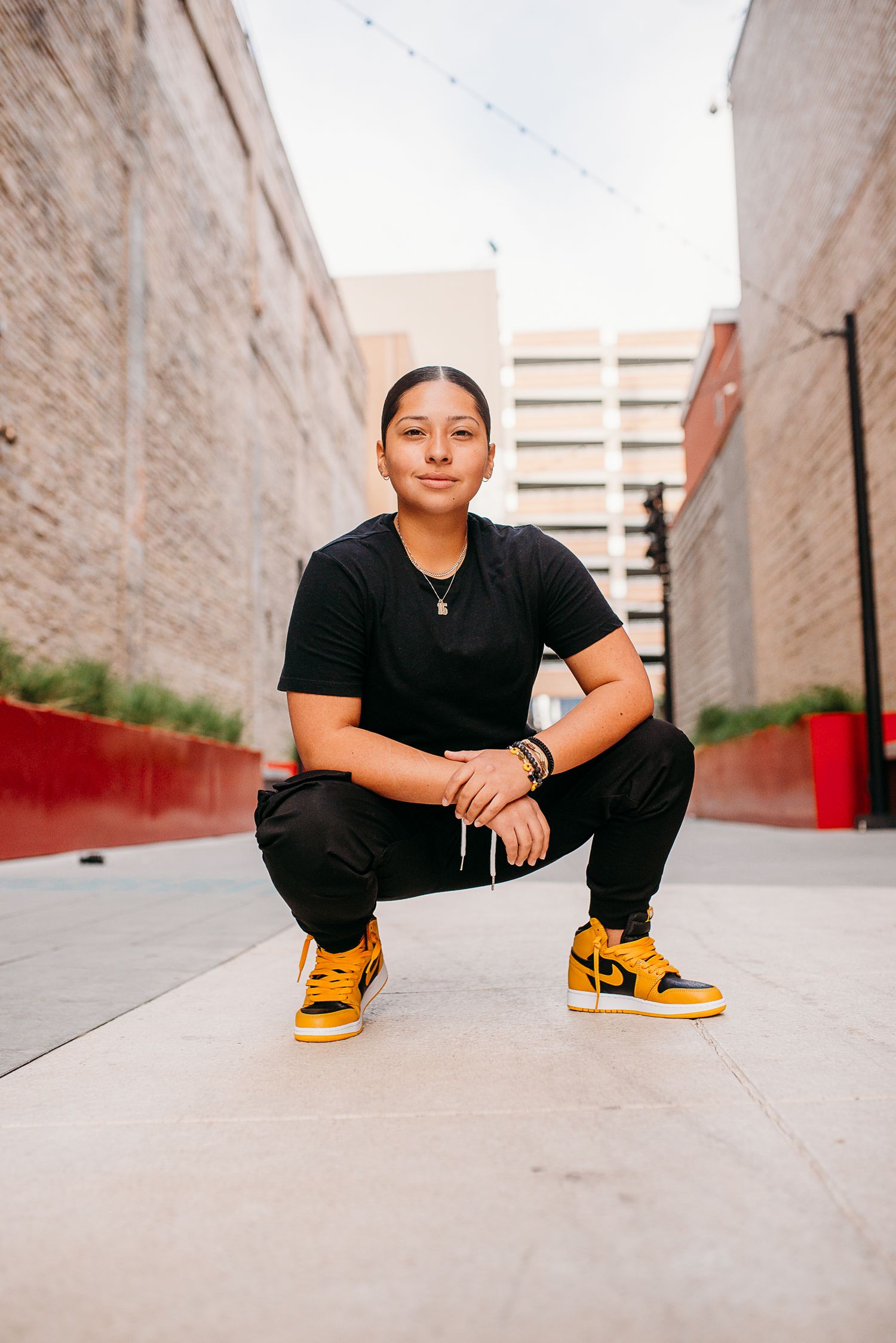 Person in black outfit and yellow sneakers crouching in urban alley between brick walls.