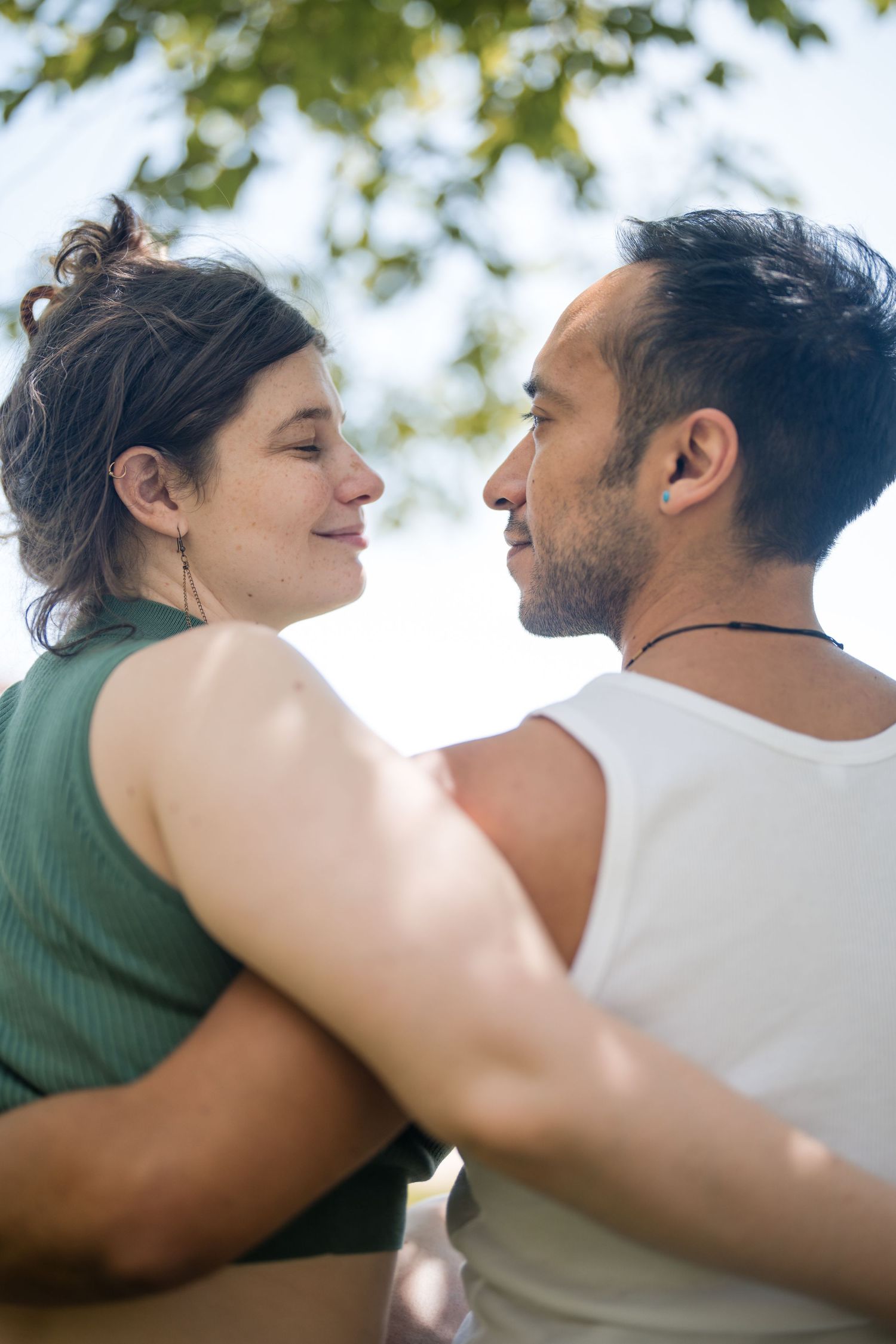 Couple embracing outdoors with soft natural lighting and green foliage in background.