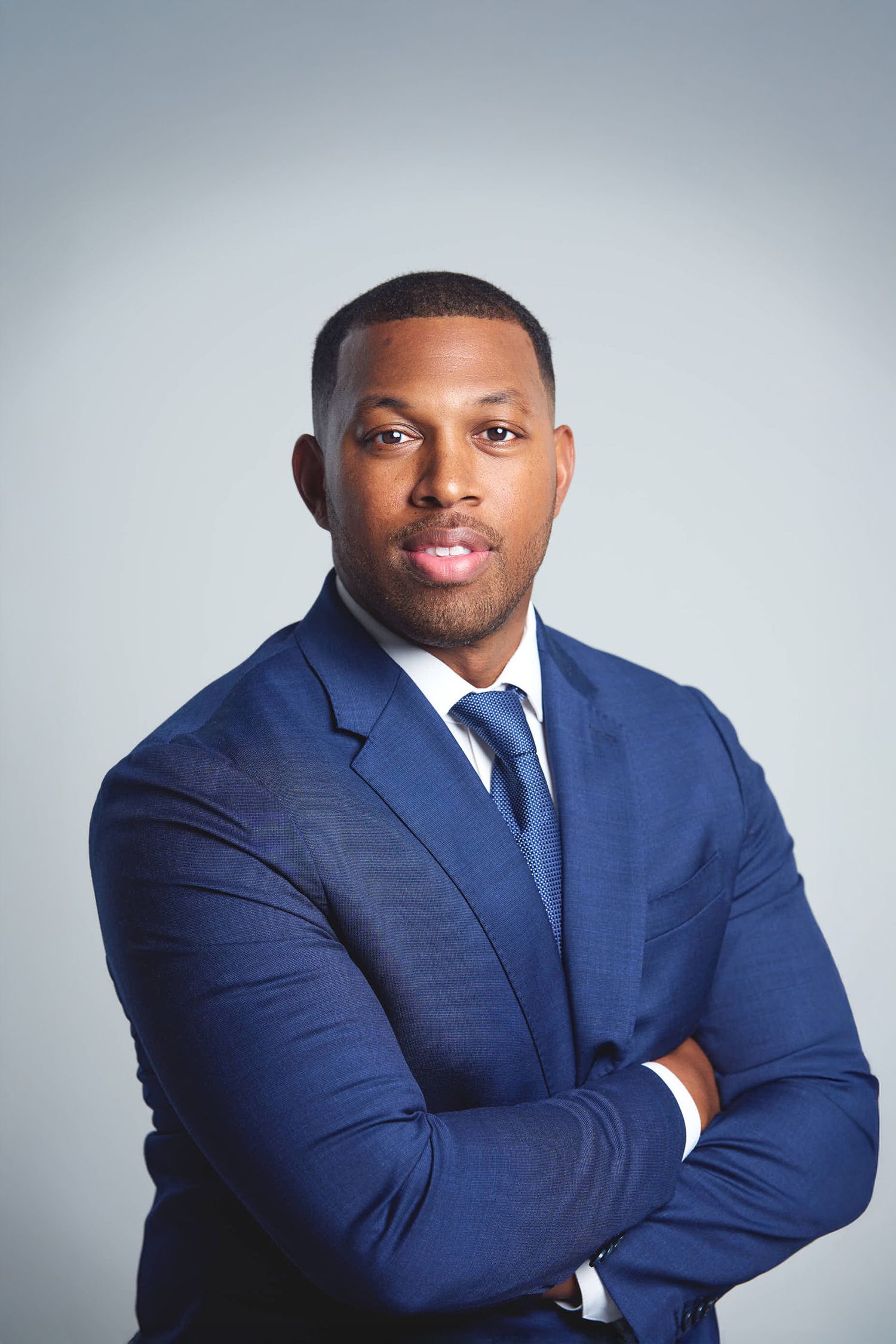 Professional headshots of a person in a navy blue suit against a gray background.