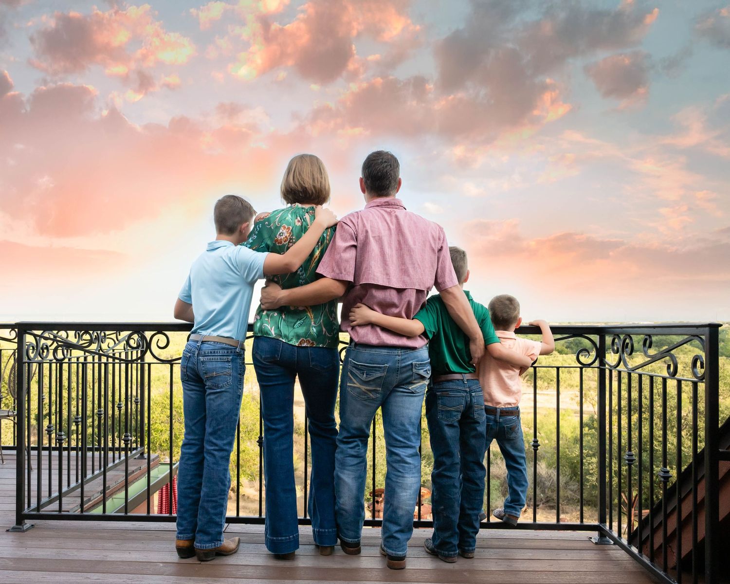 Small child in red shirt and jeans holds hands with adults while standing on blanket outdoors. family photoshoot